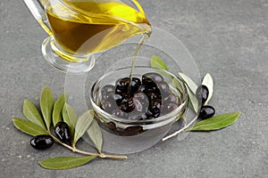 Olive oil in glass with black olives and leaves on rustic background