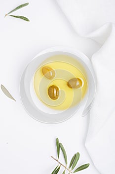 Olive oil in a glass bottle, fresh green olives in a ceramic bowl and olive branch on an old wooden table