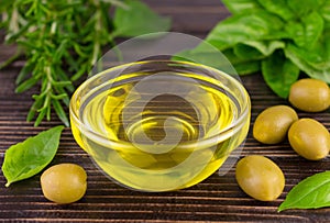 Olive oil in a glass bowl and fresh bezel and rosemary on a dark wooden background.