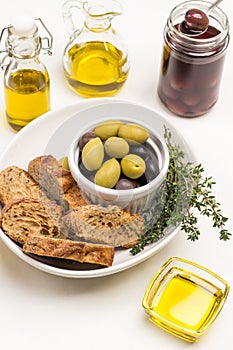 Olive oil in glass bowl. Olives, bread and thyme in ceramic bowl. Olive oil bottles