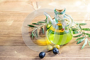 Olive oil in the glass transparent bottle, some fresh olives and olive tree branches on the wooden background in sunlights. Naturl