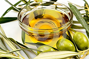 Olive oil. Greek olive oil in glass transparent bowl with olive branches with leaves and olives. Close-up on white surface