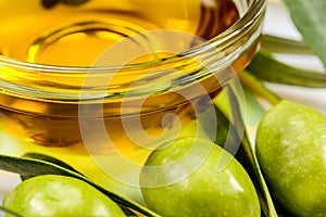 Olive oil. Greek olive oil in glass transparent bowl with olive leaves and olives. Close-up macro on white surface