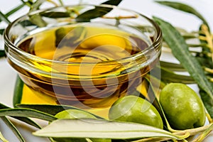 Olive oil. Greek olive oil in glass transparent bowl with olive leaves and olives. Close-up on white surface