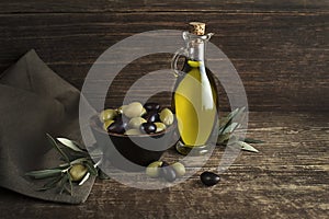 Olive oil with olives and branch on wooden background