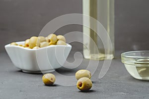 Olive oil pouring from bottle in bowl and fresh olives in ceramic plate