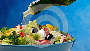 Olive oil pouring from bottle onto fresh vegetable salad