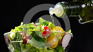 Olive oil pouring from bottle onto vegetable salad over black background