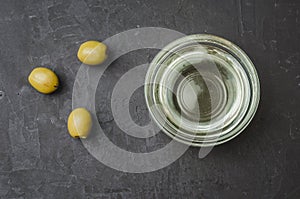 Olive oil pouring from bowl and fresh olives on dark stone background. Top view