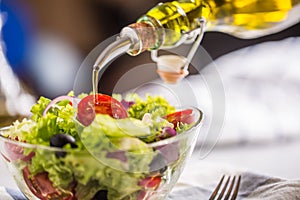 Olive oil pouring in to bowl of fresh vegetable salad