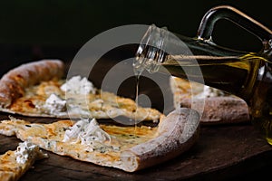 Olive oil puring on Quattro formaggi pizza on wood background