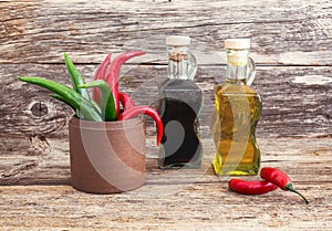 Olive oil and vinegar in glass bottles, chilly pepper on old wooden background. Toned