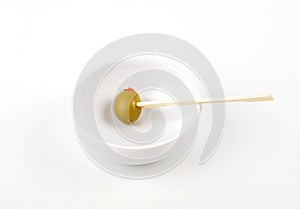 Olive with paprika on wooden skewer in porcelain bowl on white background