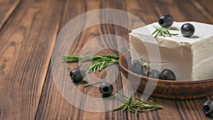 Olives on a large piece of feta cheese on a wooden table.