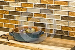 Olives in serving dish and wooden cutting board on engineered stone counter top with glass mosaic tile back splash in home kitchen