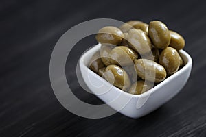 Olives in a white bowl on a dark wooden table