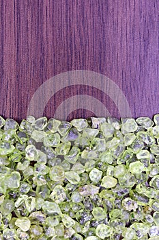 Olivine heap jewel on half brown varnished wood texture. Pile mineral pebbles background