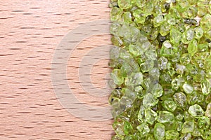 Olivine heap jewel on half light varnished wood texture. Pile mineral pebbles background.