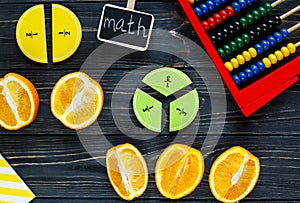 Ð¡olorful math fractions and oranges as a sample on dark wooden background or table. Interesting creative funny math for kids