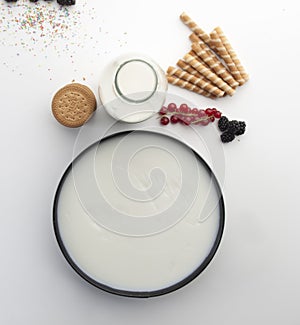 Aerial still life with a round mold filled with cream, cookies, milk bottle, gooseberries, blackberries and round wafers photo