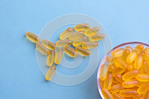 Omega 3 chewable jelly pills shaped as fish. A loty of capsules with yellow fish oil are lying on blue background.