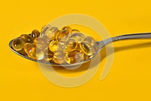 Omega-3 fish fat oil capsules in spoon on a yellow