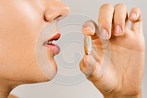 Omega 3 pill of fish fat oil near lips close-up. BADS capsule of biologically active dietary supplements. Vitamin D for