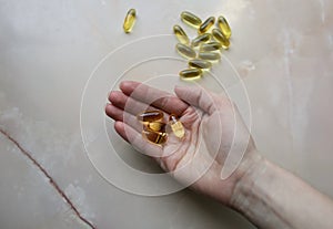 Omega 3 pills in woman`s hand on marble background. Healthy diet supplements. Fish oils for vegans food