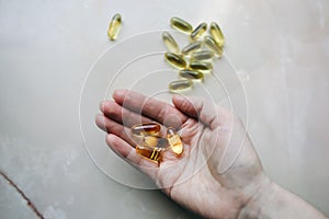 Omega 3 pills in woman`s hand on marble background. Healthy diet supplements. Fish oils for vegans food