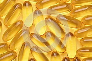 Omega 3 softgels or Fish oil capsules, yellow pills background.