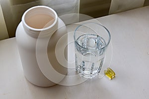 Omega-3, spirulina, chlorophyll capsules and glass of water on white wooden table. Dietary supplements, biologically active