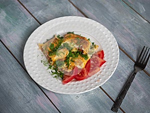 Omelet with chopped tomatoes and herbs on a white plate with a fork