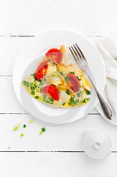 Omelet. Eggs fried. Scrambled eggs with green onion and fresh tomato. Omlette on white plate. Breakfast. Top view