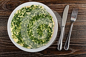 Omelet with parsley in white plate, knife and fork on wooden table. Top view