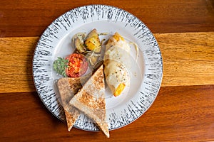 Omelet with potato, tomatoes parsley and feta cheese and bread in white plate on wooden table