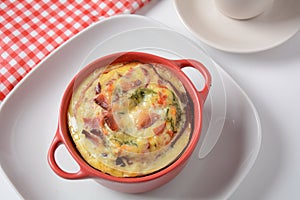 Omelette with bacon, grated parmesan and greens in ceramic cocotte.