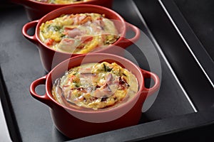 Omelette with bacon, grated parmesan and greens in ceramic cocotte.