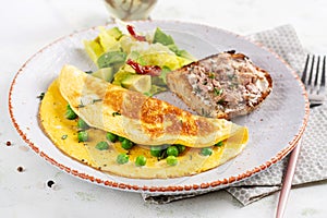 Omelette with green peas and toast with cod liver on white plate.