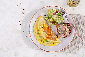 Omelette with green peas and toast with cod liver on white plate.
