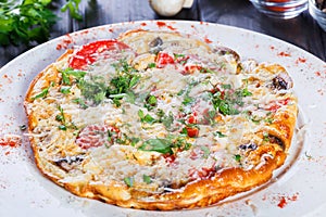 Omelette with slices ham, mushrooms, greens, cheese and tomato on dark wooden background.