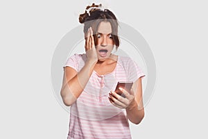 Omg, its awful! Shcoked Caucasian young female stares with bugged eyes at screen of smart phone, realized she overslept work, dres