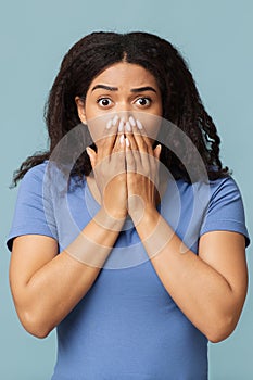 Omg. Shocked black woman covering her mouth with palms and looking at camera on blue background