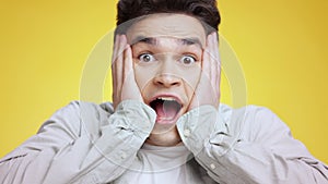 OMG, unbelievable. Close up portrait of young shocked man shouting and touching his cheeks in amazement