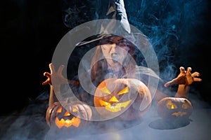 An ominous witch in a hat conjures over a jack-o-lantern. Traditional halloween characters. Mystical fog creeps over