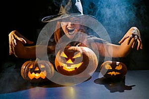 An ominous witch in a hat conjures over a jack-o-lantern. Traditional halloween characters. Mystical fog creeps over