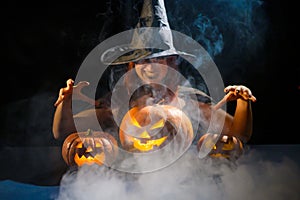 An ominous witch in a hat conjures over a jack-o-lantern. Traditional halloween characters. Mystical fog creeps over