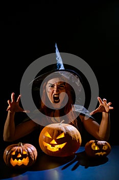 An ominous witch in a hat conjures over a jack-o-lantern. Traditional halloween characters. Mystical fog creeps over