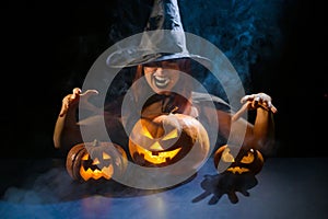 An ominous witch in a hat conjures over a jack-o-lantern. Traditional halloween characters. Mystical fog creeps over photo