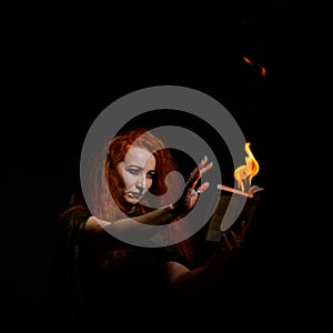 An ominous witch sets her spell book on fire with the power of thought. Red-haired woman conjures for Halloween. Flames