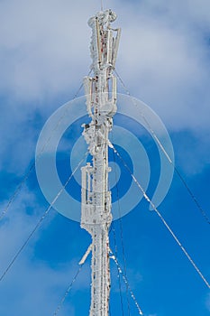 Ð¡ommunication tower covered by ice and snow on blue sky background